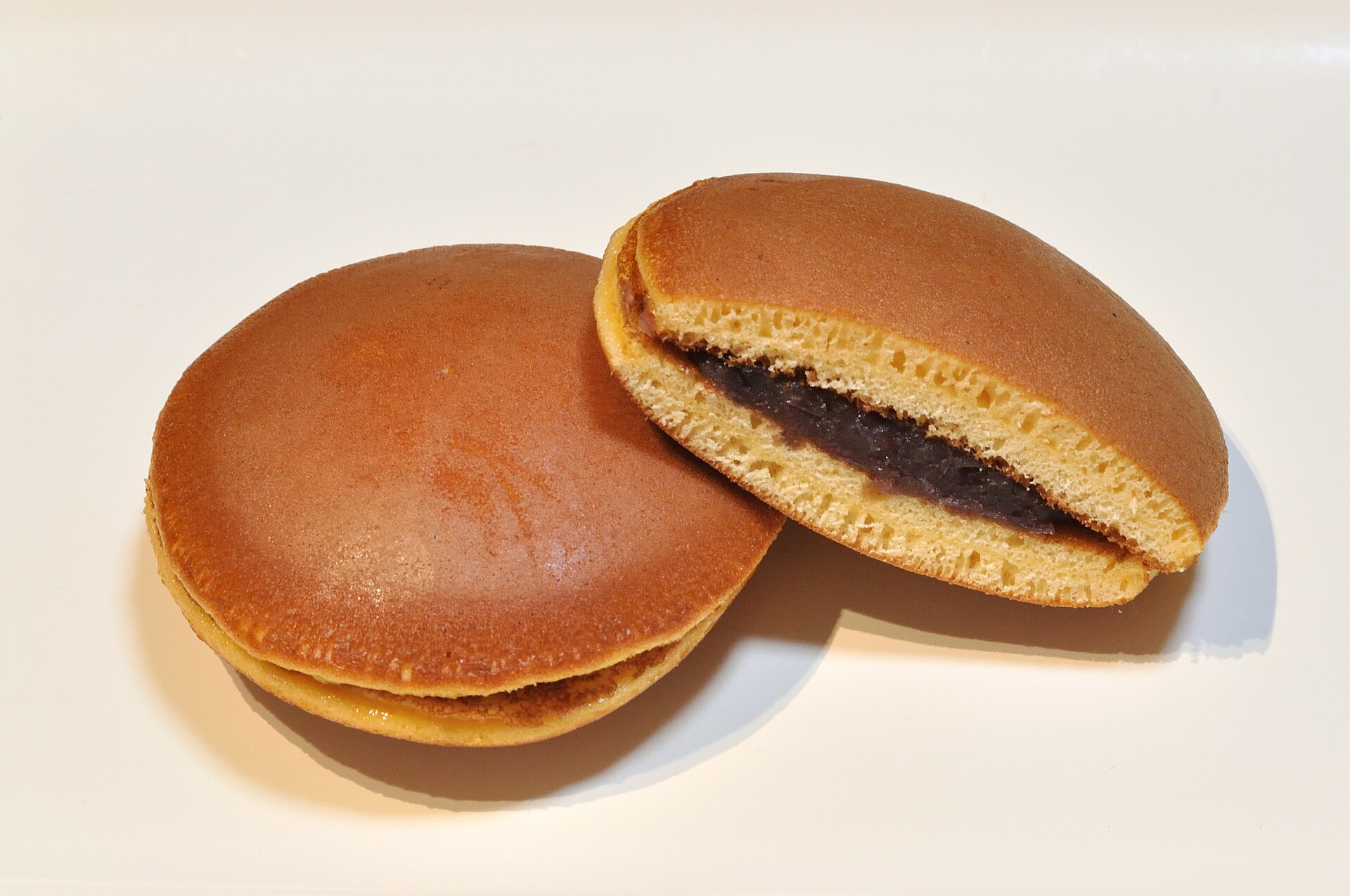 Classic dorayaki with one cut open showing chunky tsubuan red bean paste between two golden pancakes