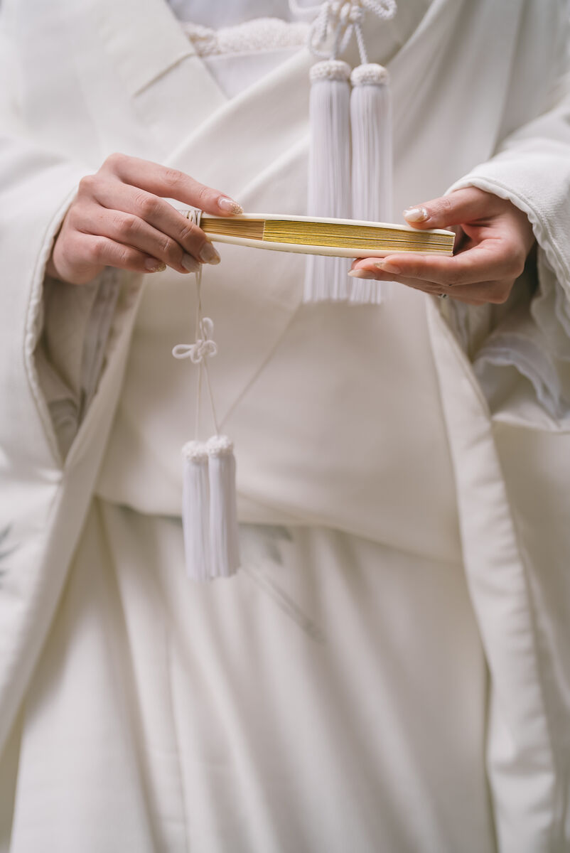 Hands holding a golden hakoseko bridal accessory on white kimono