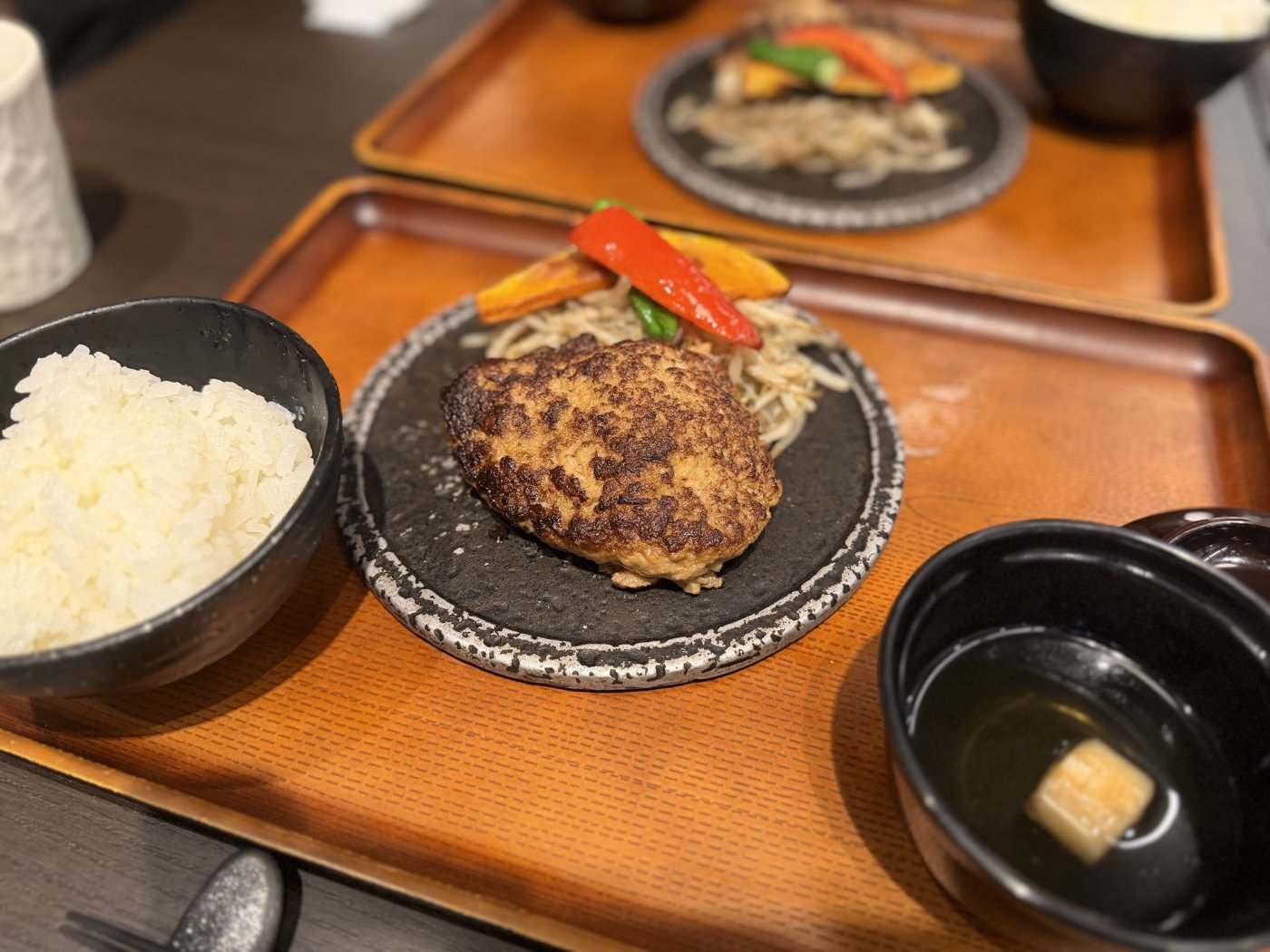 Hambagu steak on a hot stone plate with rice and miso soup on a wooden tray