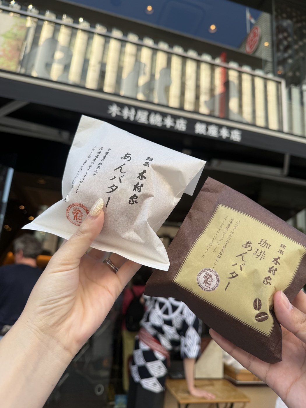 Two Kimuraya an-butter buns held up in front of the Kimuraya Ginza main store