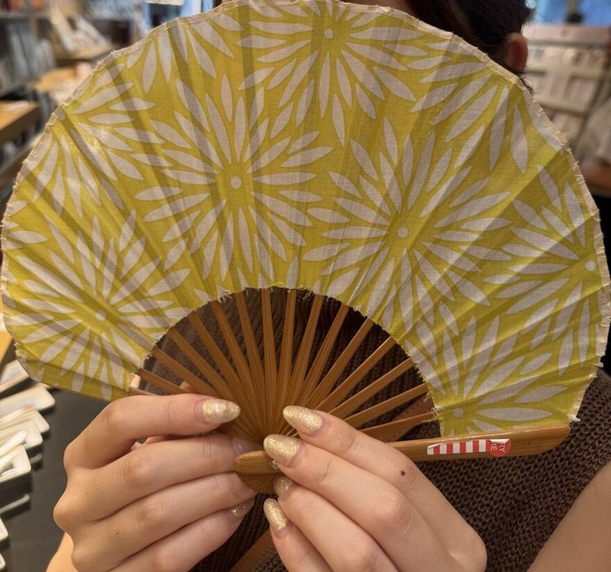 A yellow chrysanthemum-patterned sensu folding fan held open in both hands at Ginza Itoya