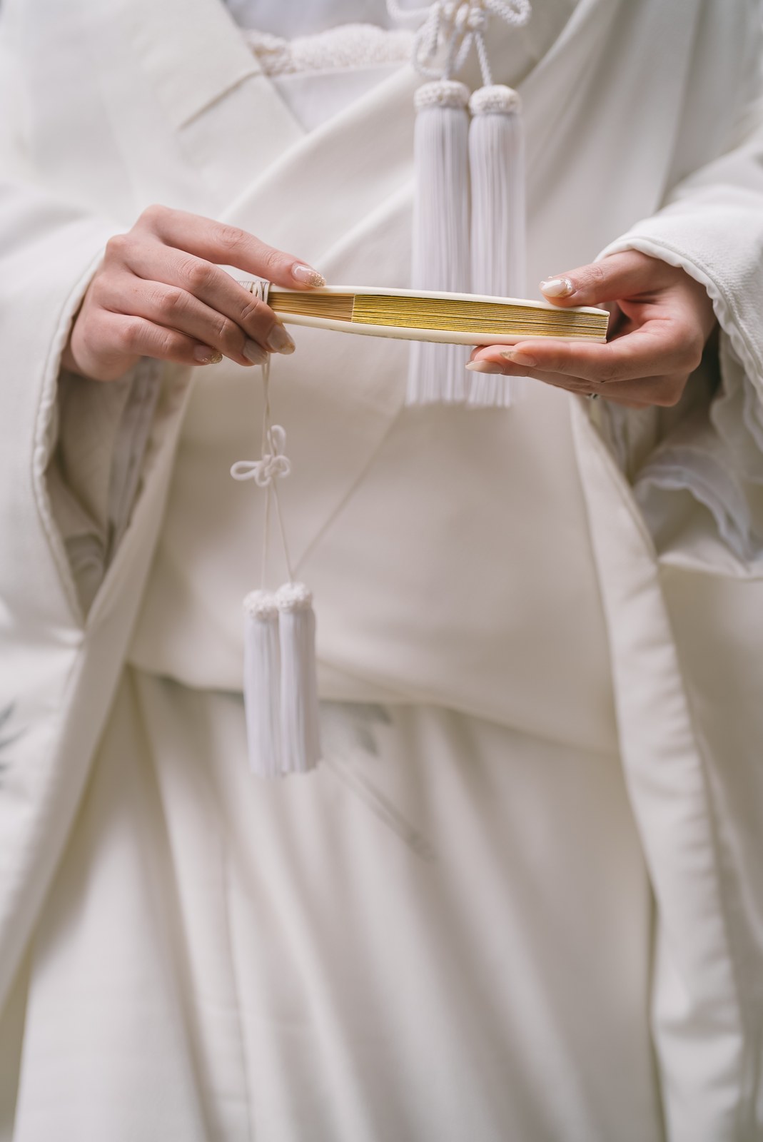 Hands holding a suehiro fan and kaiken dagger against a white shiromuku kimono