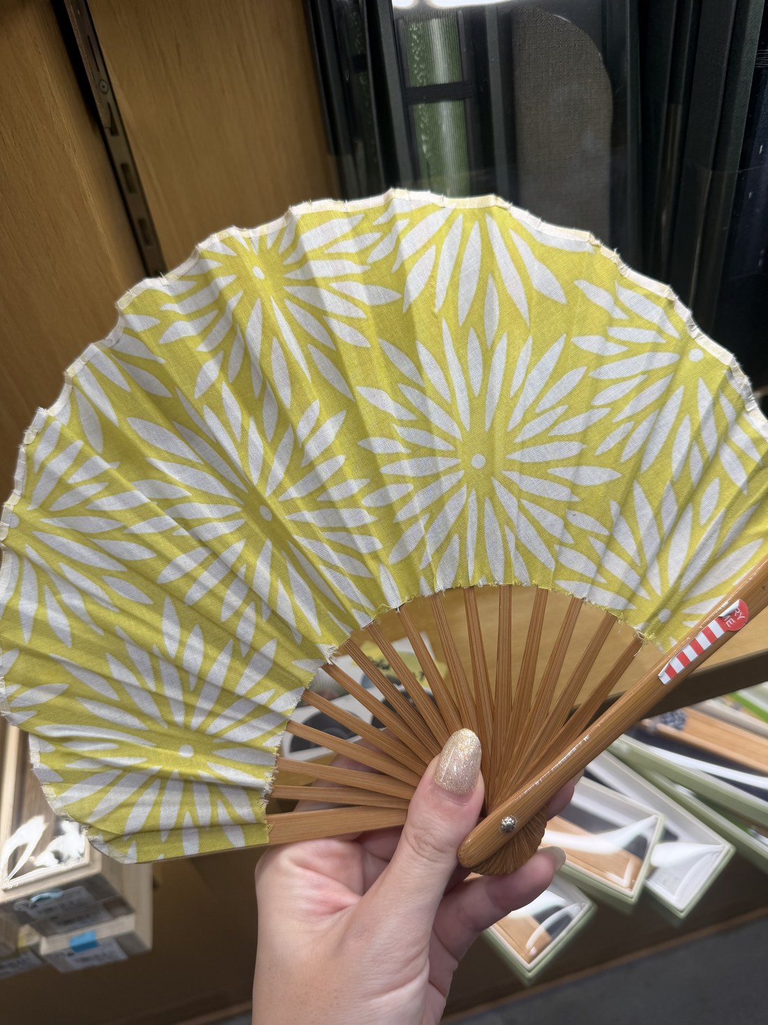 Hand holding a yellow tenugui fabric folding fan at a stationery store