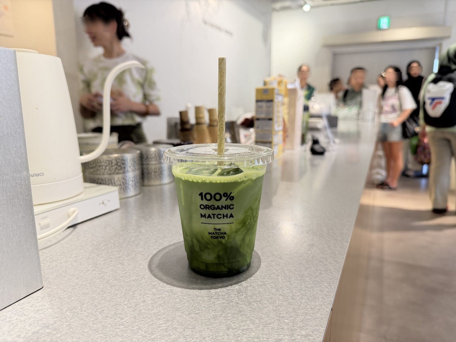 Iced matcha on the counter at THE MATCHA TOKYO with bamboo chasen whisks, kettle and customers in line