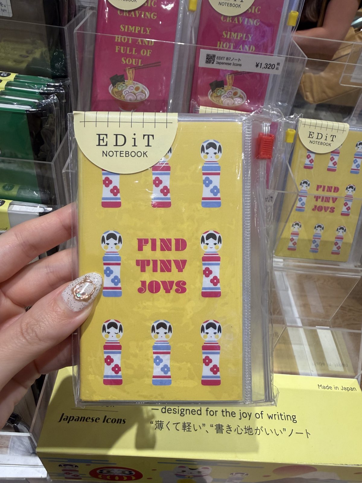 EDiT B7 notebook with a yellow kokeshi doll cover reading Find Tiny Joys held in a hand at Ginza Itoya, price tag 1320 yen