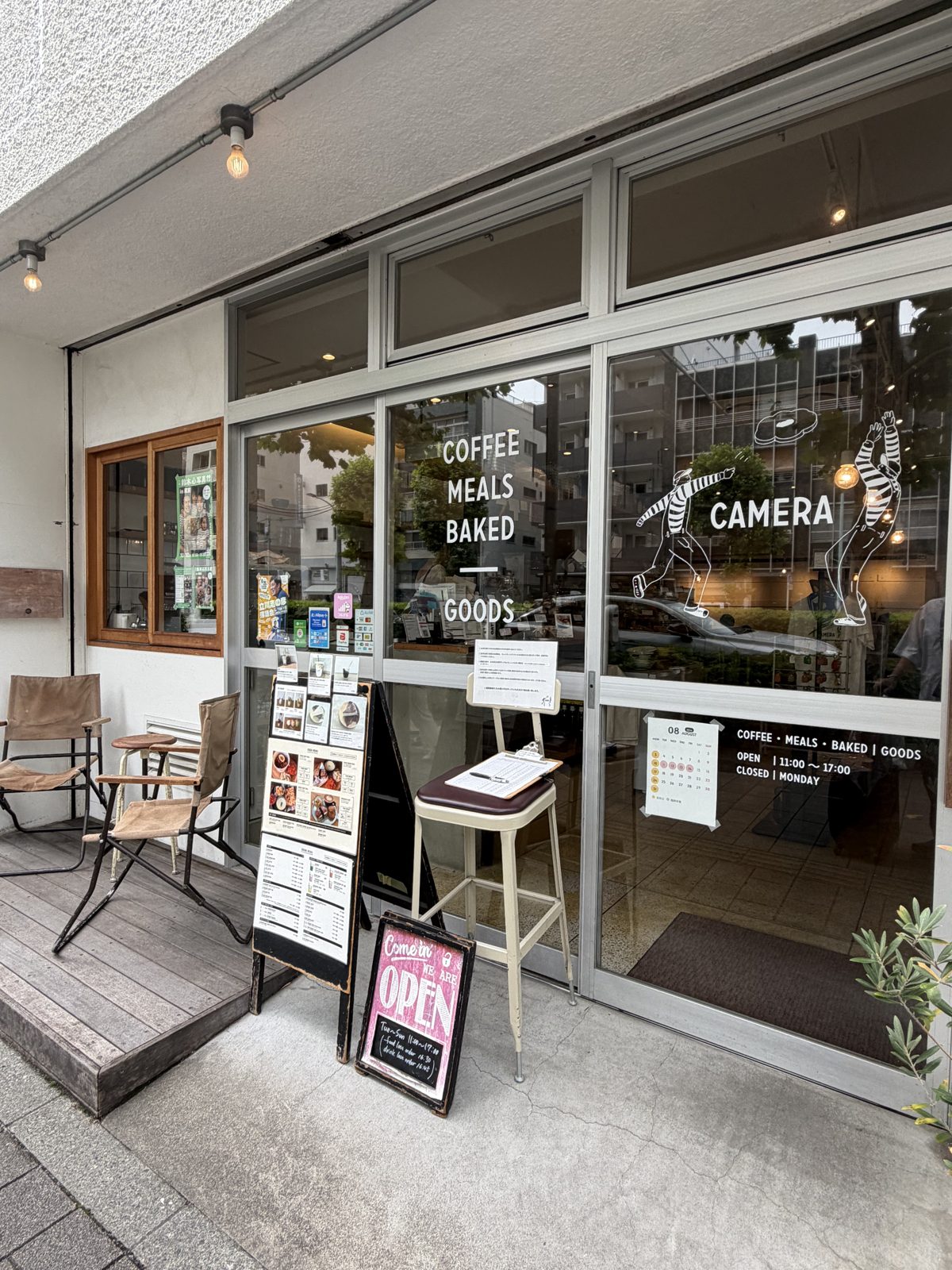 Entrance of CAMERA cafe in Kuramae Tokyo with a sign reading coffee, meals, baked, goods and an open board