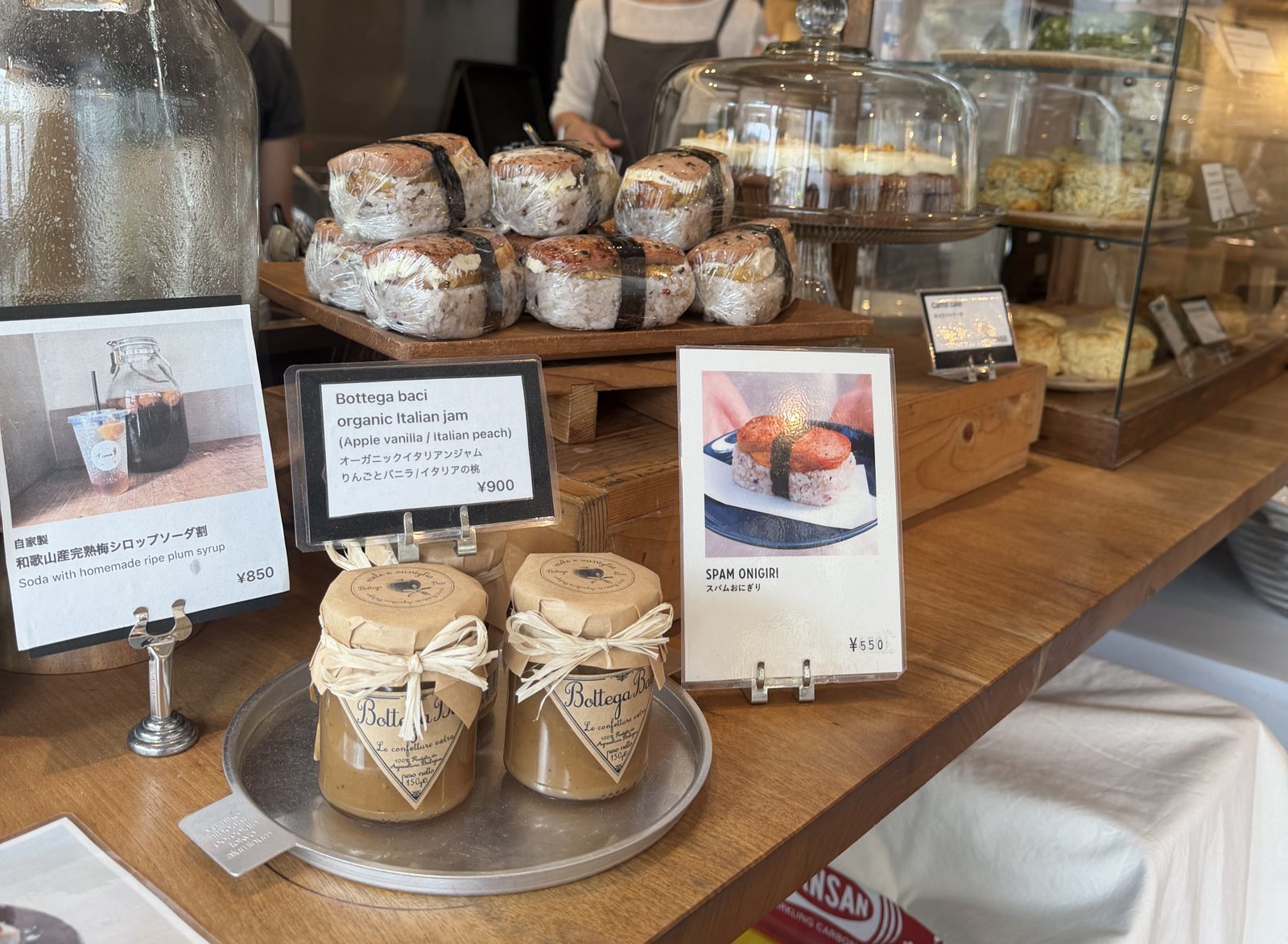 Counter at CAMERA cafe Kuramae with wrapped Spam onigiri rice balls, price cards for spam onigiri 550 yen, plum syrup soda 850 yen and organic Italian jam 900 yen