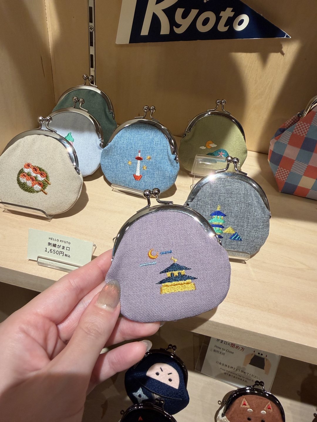 Hand holding a purple embroidered gamaguchi coin purse with the Golden Pavilion, price card ¥1,650